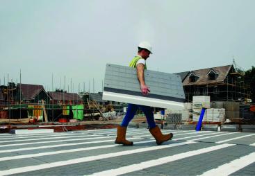 A man in PPE walks across new floor made from Milbank Concrete Products' GDeck, while carrying a panel of the lightweight flooring system.