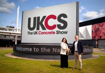 Richard Bradbury (right), Managing Director of The QMJ Group with Helaena Ackers, Exhibition Sales Account Manager, The NEC shake hands outside the NEC in front of a huge UK Concrete Show sign, following the signing of a two-year deal that sees the flagship trade show to stay at Birmingham’s NEC through 2027, with free parking and expanded plans for 2026 edition
