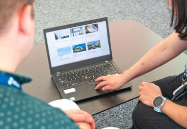 Two people look at a laptop screen which shows several photos and text related to sustainable construction
