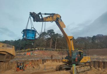 A yellow excavator lifts a blue pile cropper at the Port of Nigg, Scotland