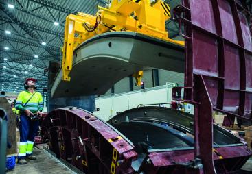 A yellow and blue PPE clad worker in a factory uses a mould and lifting device for precast tunnel segments, France, CBE