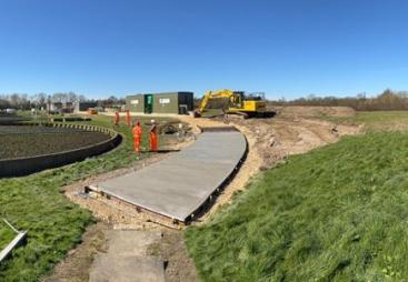 A waste water treatment plant with a CoMLaG mix access road in the foreground surrounded by grassy banks