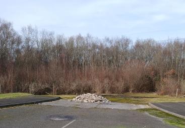 A dead-end road with a pile of illegally dumped concrete hardcore, with trees in the background.