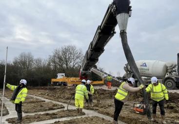 construction workers in yellow PPE lay concrete that's being delivered via chute from a concrete mixer