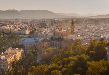 A panoramic photo of Malaga city centre with mountains in the distance, with the bullring lower right and a large church middle left.