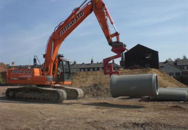 An orange excavator lifts a concrete pipe