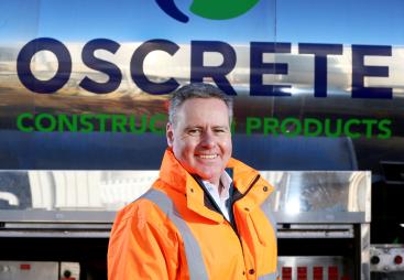 Oscrete director Scott Wilson stand in front of an Oscrete sign wearing orange PPE