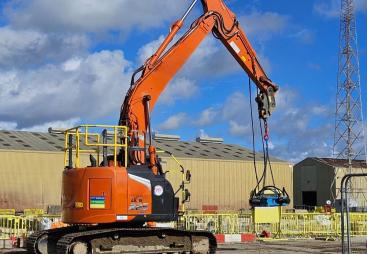 An orange, zero tail-swing midi excavator lifts a pile cropper on a construction site