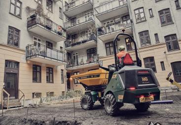 A yellow site dumper being driven in front of an urban construction site