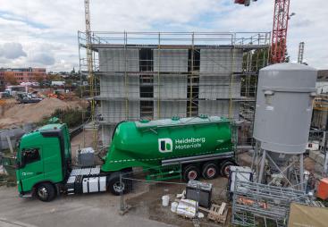 A green, Heidelberg Materials' cement truck in front of an under construction house
