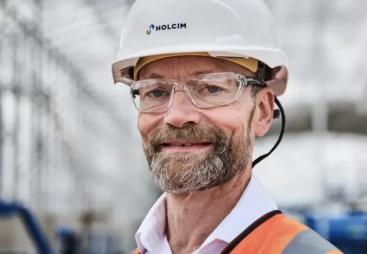 A head and shoulders photo of a man with a beard and glasses wearing PPE and a white hard hat