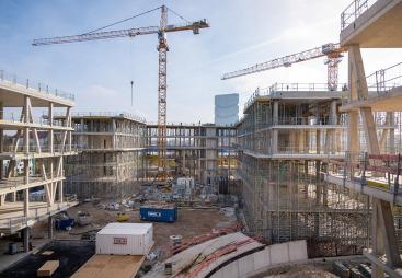 An under construction mid-rise building with two tower cranes in the background