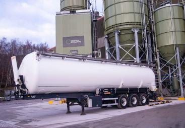 A white, material tanker standing in front of Material Evolution’s Mevo A1 Production Facility in Llay, Wrexham – the UK’s largest producer of ultra-low carbon cement, with a capacity of 120,000 tonnes per year.