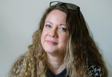 A head shot of Laila Morris, newly appointed practice director at Betts Associates, with long curly hair, a checked top and glasses on her head