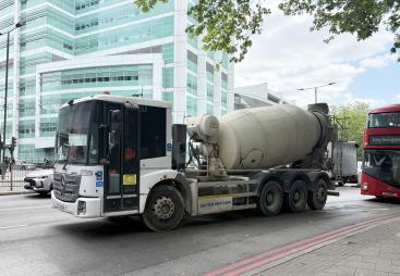A concrete mixer drives along a street in London with a red double decker following 