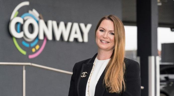 A woman standing in front of FM Conway's logo