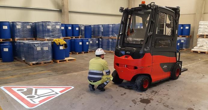 A man in a factory crouching down in front of a forklift