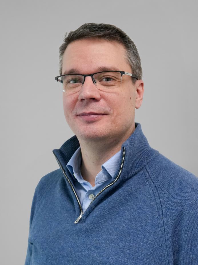 Head and shoulders picture of a man in a blue jumper and glasses