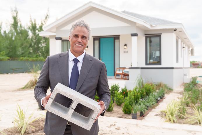 A man holding a concrete block outside a small house