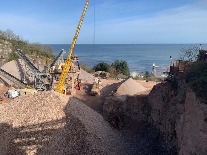 A picture of a yellow crane in a quarry with the sea in the background