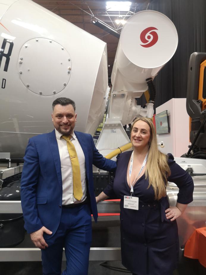 A man and a woman stading in front of a concrete mixer