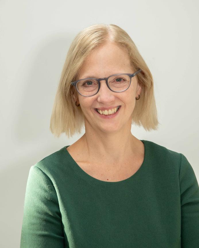 A head and shoulders picture of a blond haired woman in glasses and a green jumper