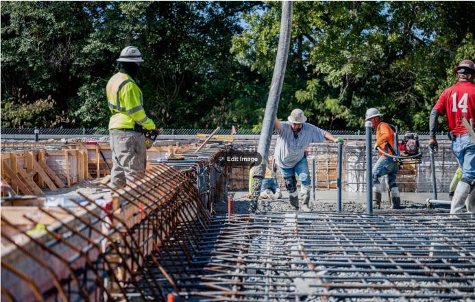 Four US construction workers in bright tshirts and PPE pour concrete