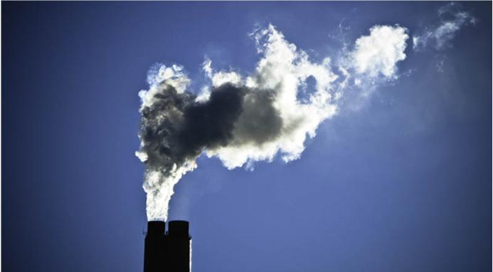 The top of a smoking industrial chimney with black and white smoke billowing from the top