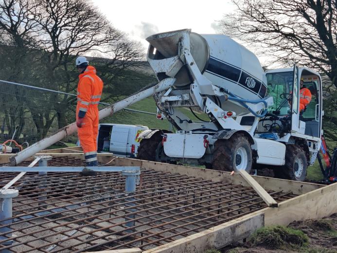 A mobile concrete mixer pouring concrete in a rural locartion with a man in bright PPE
