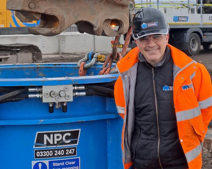 A man in orange PPE standing in front of a blue metal cylinder
