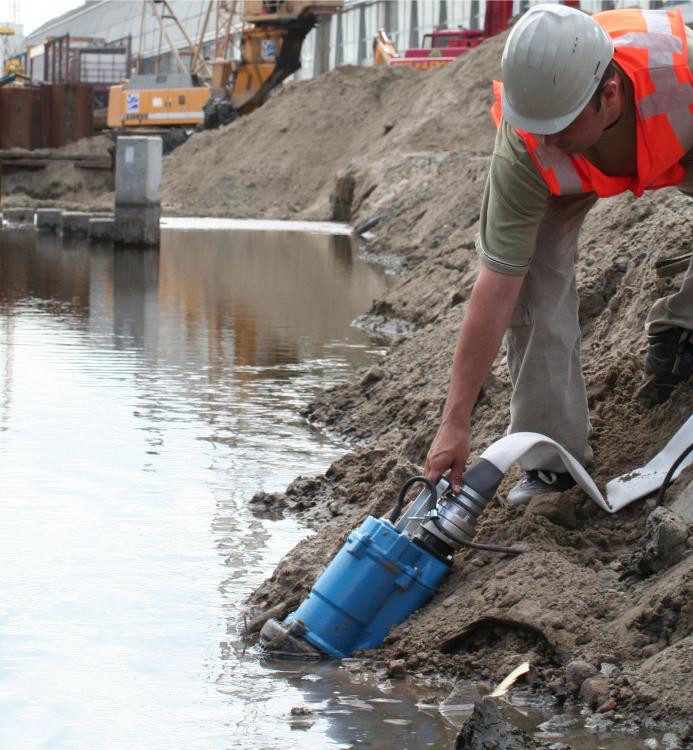 A man in red PPE holds a dewatering pump in water