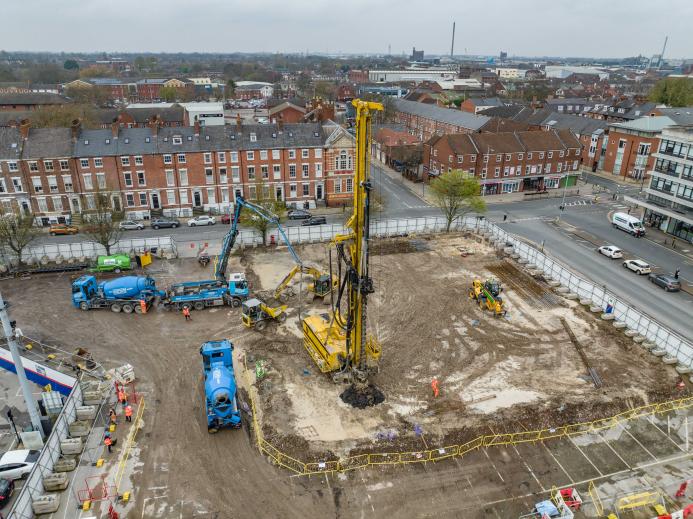 An aerial photo of a construction site with blue concrete mixers and concrete pump, and a yellow foundation rig