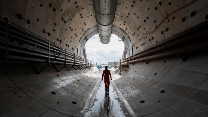 A man in yellow PPE silhouetted against the entrace to a concrete lined tunnel 