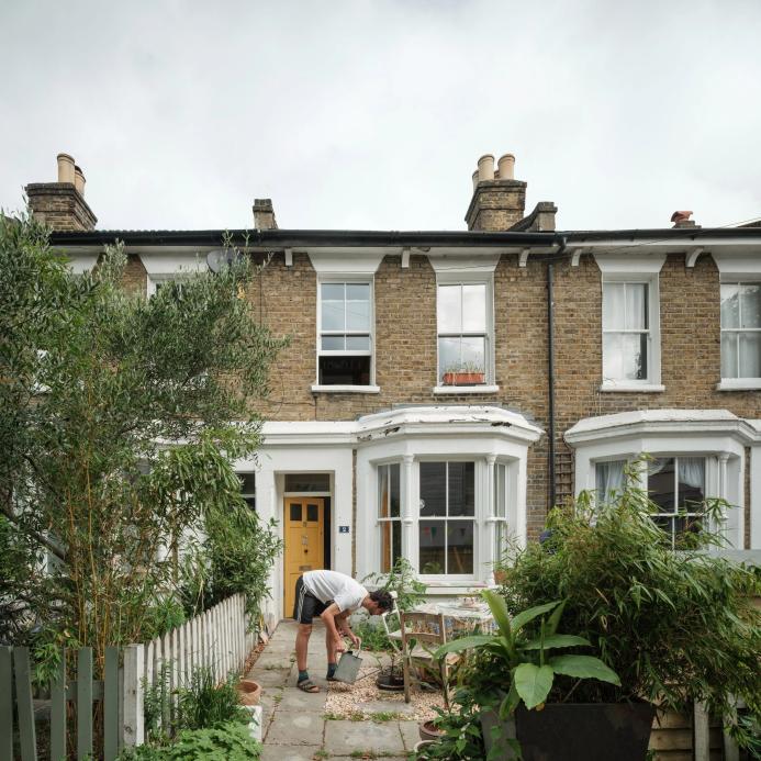 A man in shorts working in the front garden of a victorian terrace house