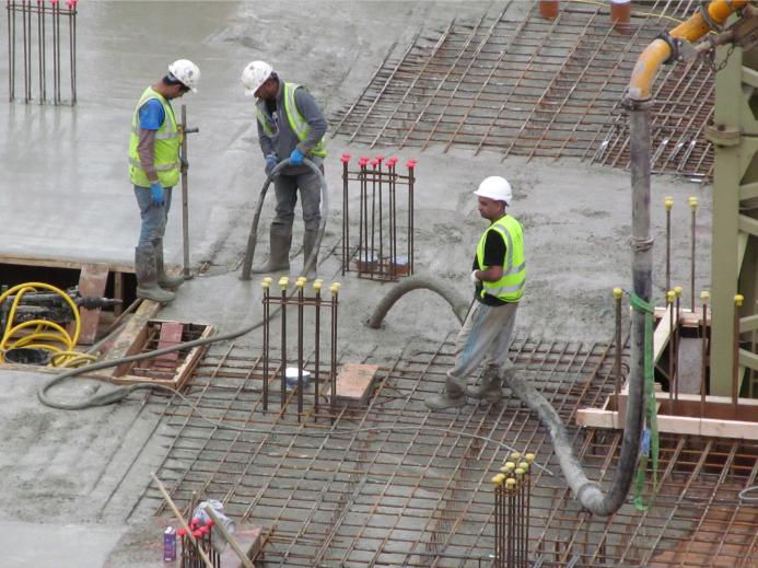 Three UK construction workers in PPE using a concrete pump to place concrete