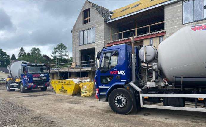 Two blue and grey concrete mixer trucks outside a new build house