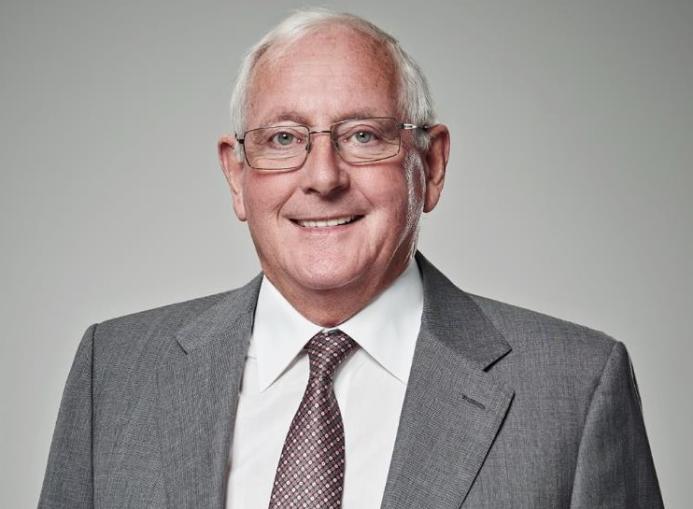 A head and shoulders picture of an old man in a grey suit and tie wearing glasses