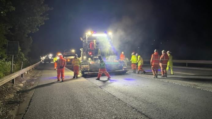 People in PPE repair a road at night