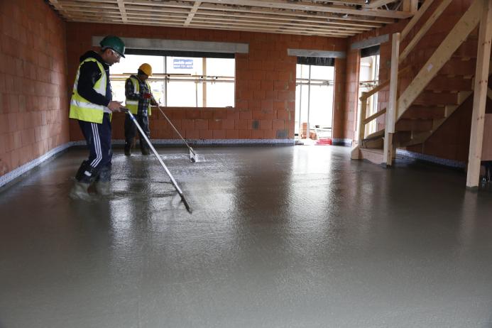 Two men in yellow PPE using screeds to level and internal concrete floor