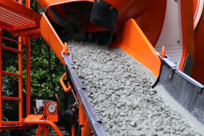 A close up of an orange cement mixer's chute discharging concrete