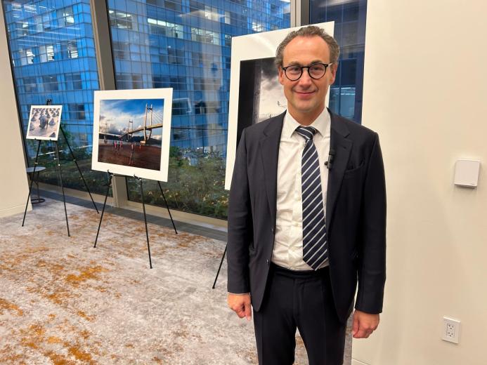 A man in suit and tie, with glasses stands in front of several photos on an easels