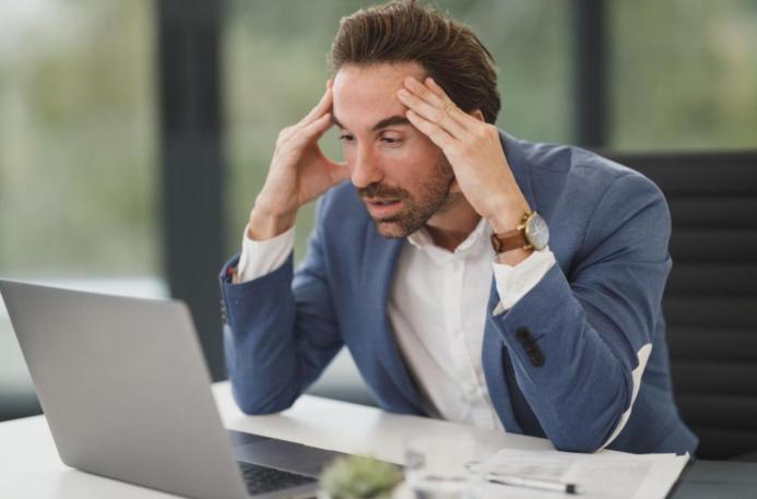 Stressed man working on a laptop in office. A businessman appears stressed and overworked in front of his laptop