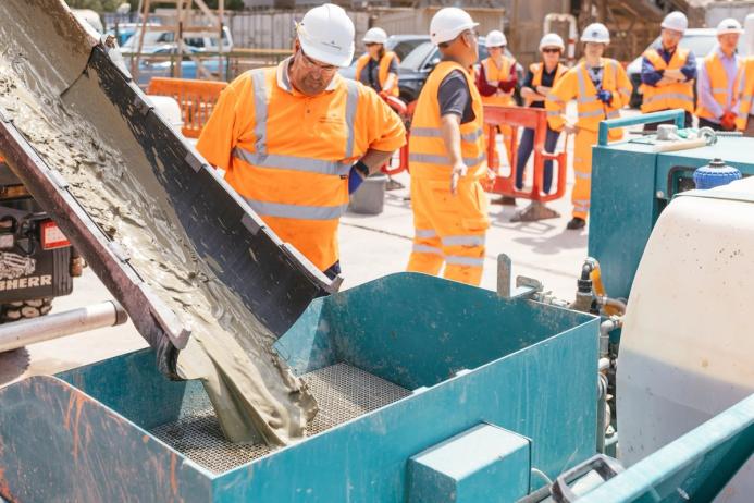 Men in orange PPE watching concrete being poured