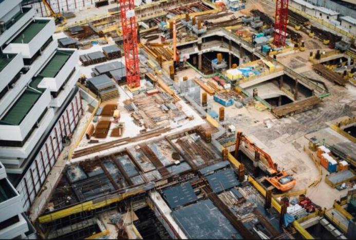 A costruction site with several peices of equipment including a red tower crane and a yellow excavator