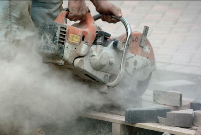 A close up of a hand-held concrete saw in use with silica dust clouds