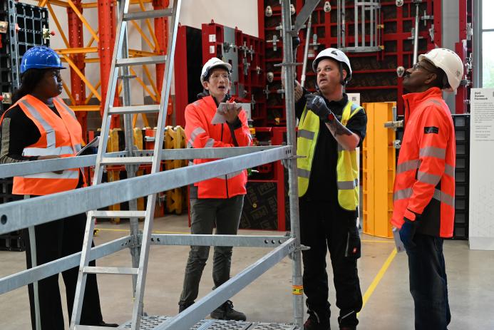 Three men in orange PPE and one in yellow inspect scaffolding