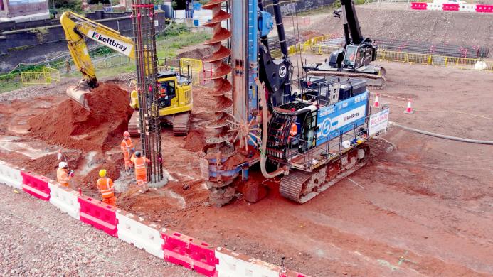 A blue piling rig and a yellow excavator at work on a construction site