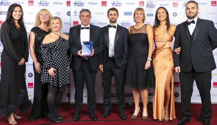 A group of people in evening wear in a line, on a stage accepting an award