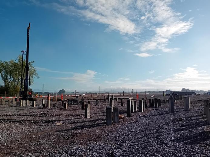 A piling rig stands surveying a filed of concrete piling caps