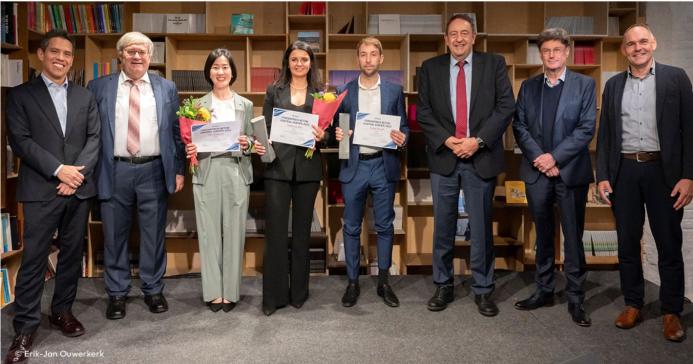 A line of people, some of whom are holding certificates,  standing in front of shelves celebrate winning the 2024 Förderpreis Beton Central Europe Competition
